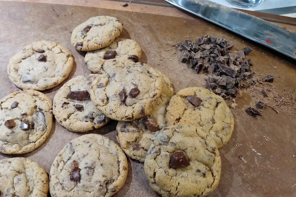 Des cookies aux pépites de chocolat et un petit tas de chocolat haché sur une planche à découper
